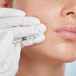 Closeup of woman getting lip fillers or botox. Young caucasian model isolated against a grey studio.