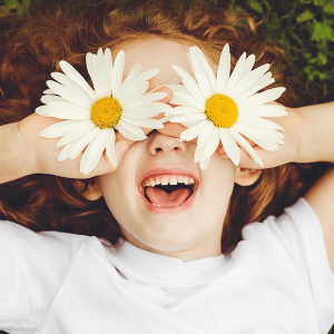 Smiling child with daisy eyes, on green grass.